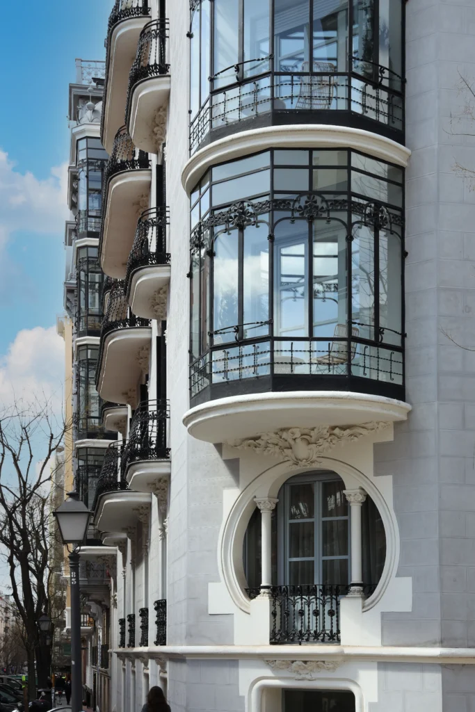 Elegant white building with curved glass bay windows and decorative black wrought-iron balconies along a street