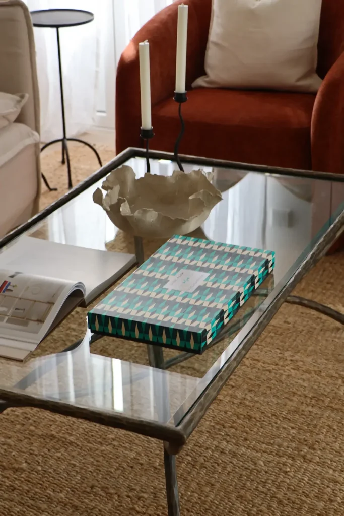 Detalle de la mesa de centro de cristal y forja con libro y centro decorativo, junto a una butaca terracota